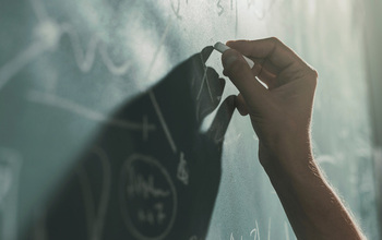 A hand writing equations with chalk on a chalkboard.